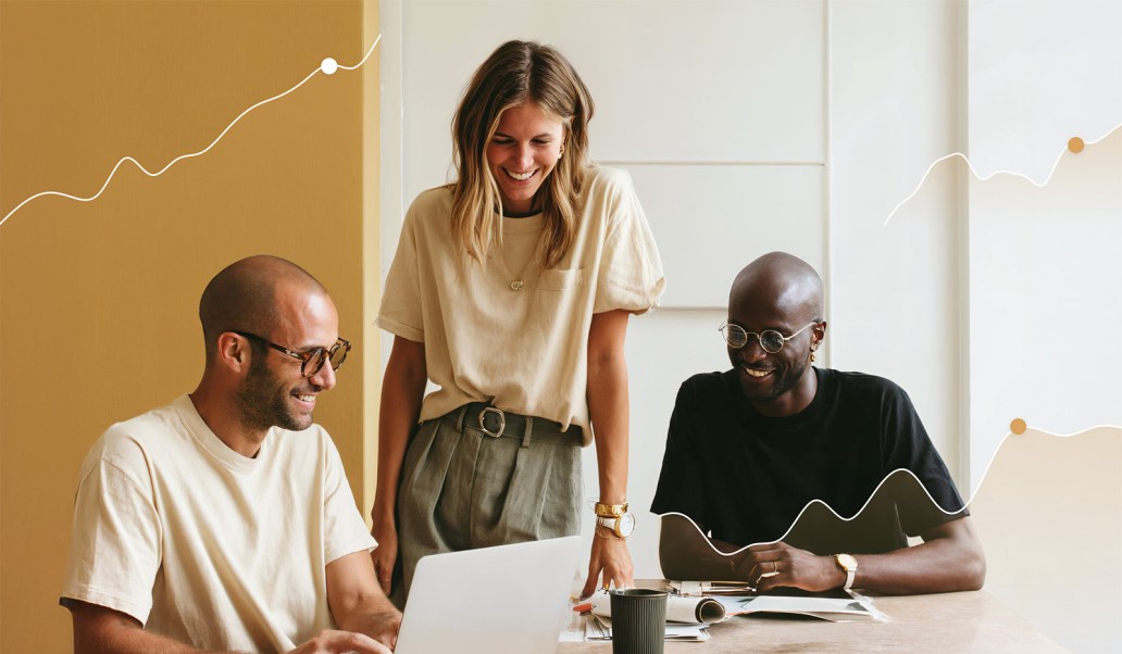 Three colleagues smile and collaborate around a laptop at a sunlit desk. Two men sit while a woman stands between them, all casually dressed. Curved data-like lines with dots overlay the image, symbolizing growth or collaboration metrics.
